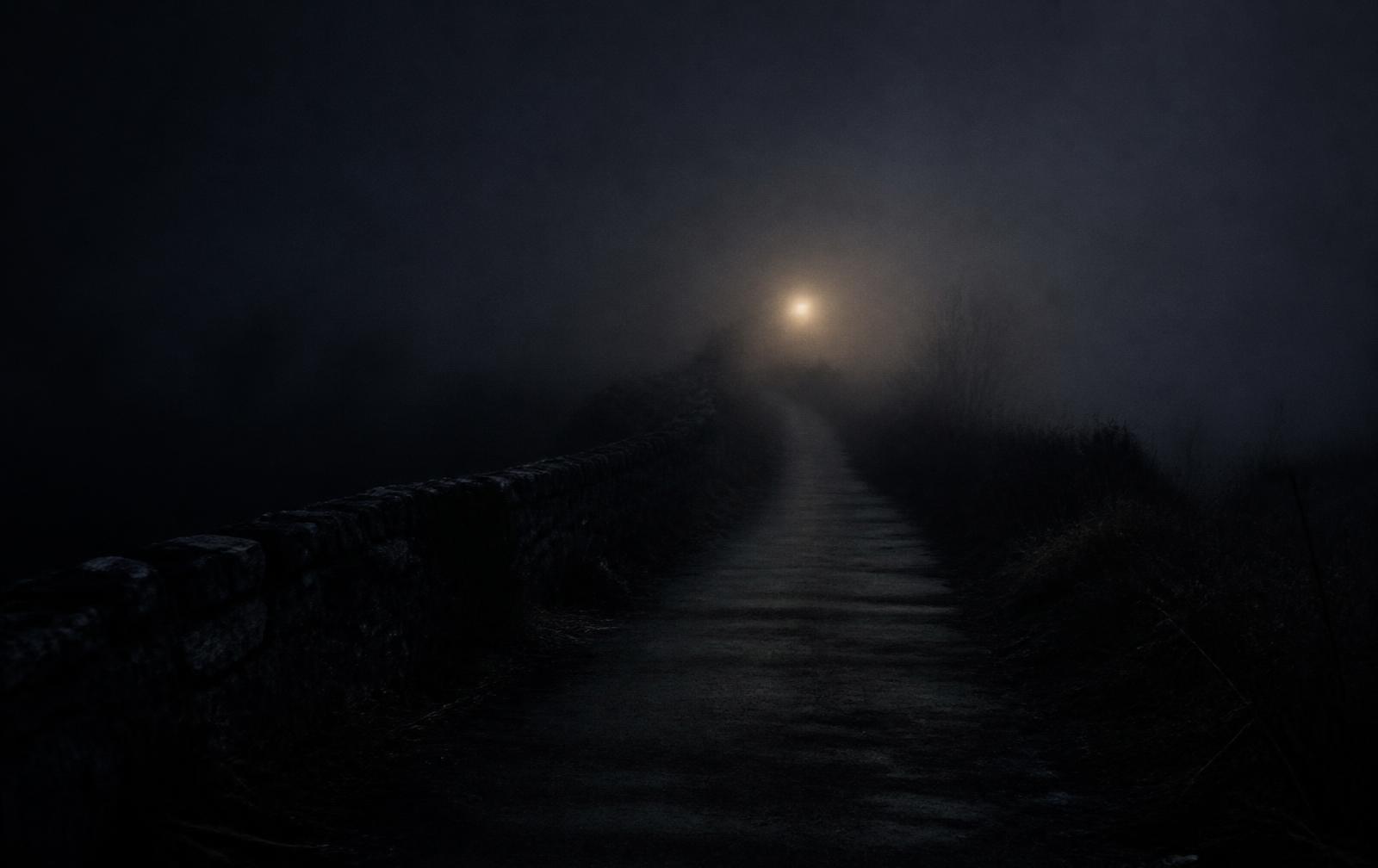 An empty path fading into thick night fog with a faint light in the distance